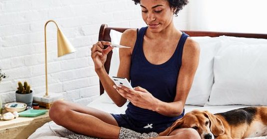 A woman taking a test sitting on her bed with her phone in one hand