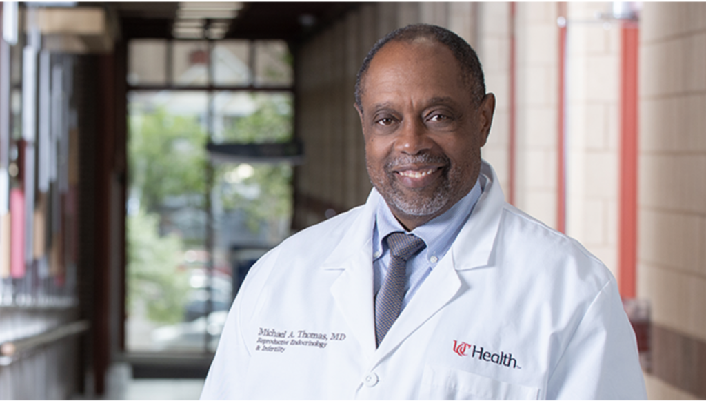 A professional headshot of Dr. Michael A. Thomas of UC Health wearing a medical lab coat and smiling in a clinic hallway