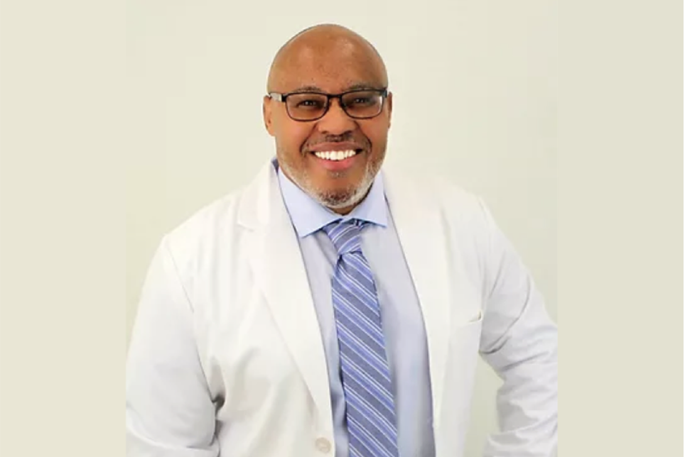A professional headshot of Dr. Melvin Thornton of Extend Fertility wearing a white lab coat and purple tie